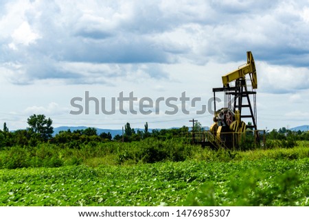 Oil rig pumps oil against the backdrop of mountains and overcast sky. Beautiful mountain landscape. Lead clouds hang over oil field.  Place for text.