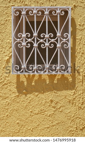 Yellow painted wall with a white iron nostalgic window decoration and organic shapes in the summer