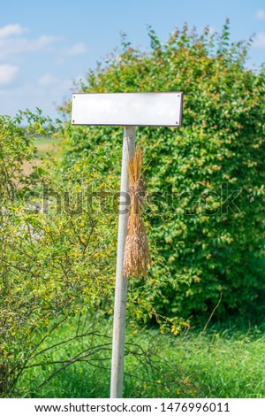 Empty blank sign post with no text. Green countryside background with blue sky. Sheaf of wheat attached to sign