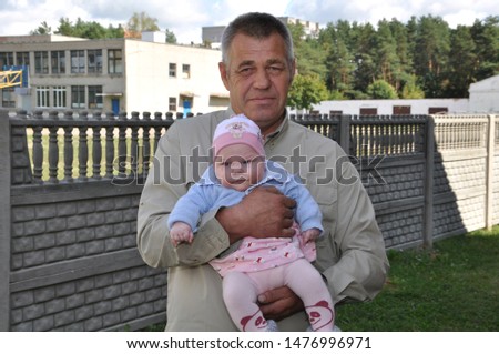 An elderly grandfather holds a small child in his arms.
