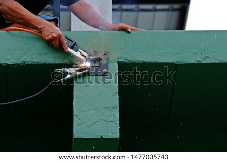 Worker using electric welding to connect angle iron into steel plate with smoke and spark of fire.