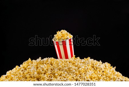 Paper striped bucket installed on scattered popcorn isolated on black background, concept of watching TV or cinema.