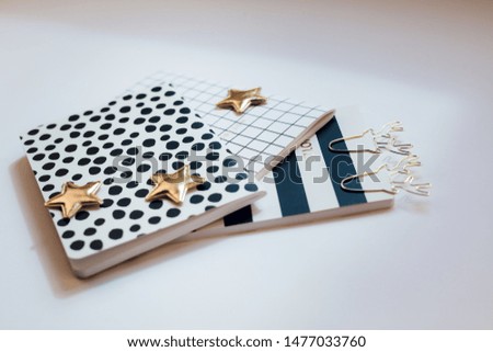 Desktop feminine composition with patterned notepads, golden stars and deer clips on white table with sun light and shadows. 