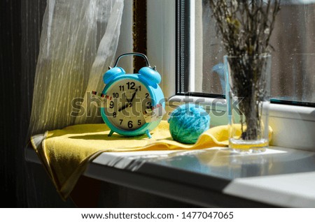 bright blue alarm clock on the windowsill morning with flowers. good morning