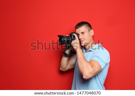 Young professional photographer taking picture on red background. Space for text