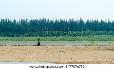 The girl-traveler on the edge of an abandoned stone pier sits resting and taking pictures on the phone in the North of Yakutia near the vilyu river.