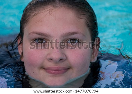 Young teenage girl in a pool in flat light looking at the camera and acting silly. Summer fun concept shot