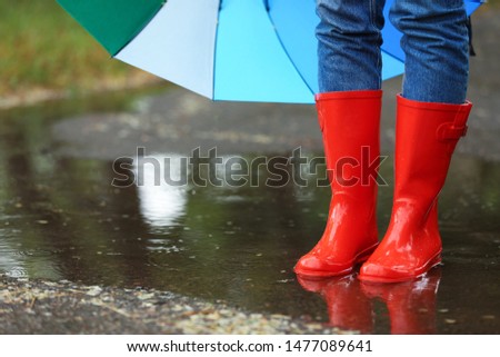 Woman with umbrella and rubber boots in puddle, closeup. Rainy weather Royalty-Free Stock Photo #1477089641