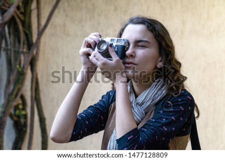 Young pretty girl taking picture with digital vintage camera in garden on sunny summer day with clear wall background. Travel, photographer, art, freedom, photography, youth and technology concept.