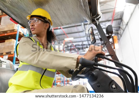 Low angle view of female staff driving forklift in warehouse. This is a freight transportation and distribution warehouse. Industrial and industrial workers concept Royalty-Free Stock Photo #1477134236