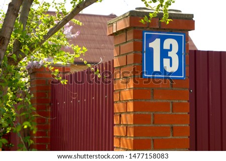 Blue color sign house number 13 on a red brick wall outdoors.Urban exterior.