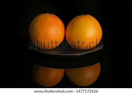 Group of two whole fresh pink grapefruit on gray ceramic plate isolated on black glass
