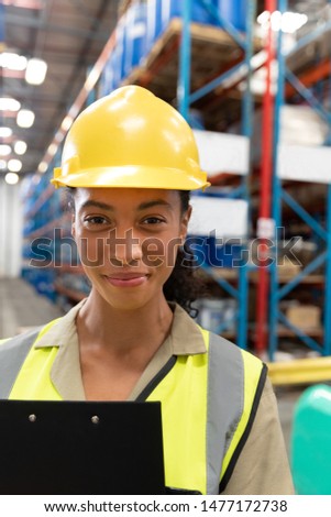 Close-up of female staff with clipboard looking at camera in warehouse. This is a freight transportation and distribution warehouse. Industrial and industrial workers concept
