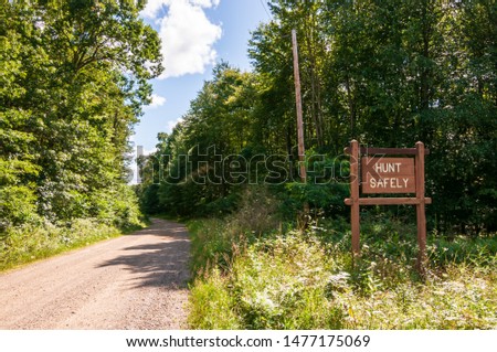 A wooden sign saying HUNT SAFELY on  the side of a dirt road in Warren county, Pennsylvania, USA on a sunny summer day