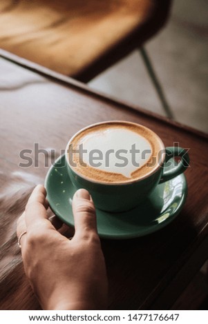 Woman holding in hand cappuccino coffee with heart latte art in turquoise cup and plate on wooden table. From above. Copyspace