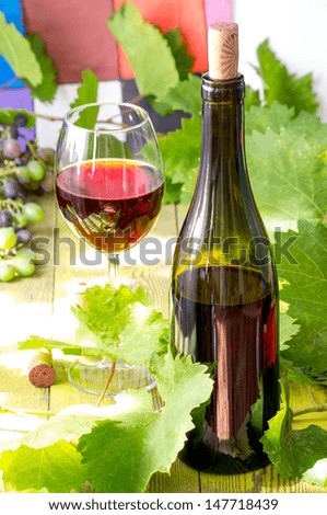 Glass of red wine on a wooden table with leaves of grapes, corkscrew and wine corks and bottle of wine and a bunch of young grapes.
