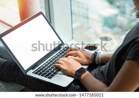  Close up of woman hands typing on keyboard. Young casually dressed female freelancer working home sitting on windowsill. Laptop with blank white screen. Mock up, copy spzce for your text.
