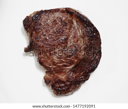 Cooked juicy ribeye steak isolated on white plate. Tasty piece of meat for food advertising. Picture for restaurant menu or trade materials. Fried beef top view.
