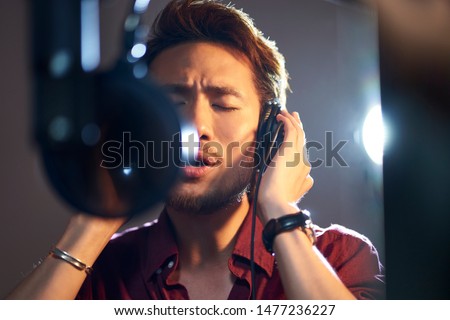 young asian adult man enjoying singing a song in modern recording studio