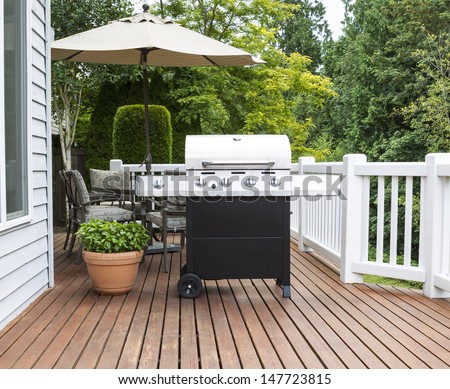 Photo of large barbecue cooker on cedar deck with patio furniture and trees in background   Royalty-Free Stock Photo #147723815