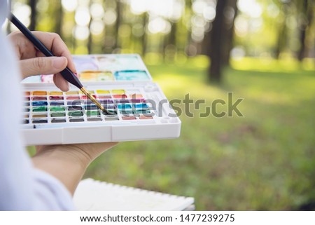 Relax woman painting water colour art work in green garden forest nature - people with creative art in nature stress reduction and meditation concept 