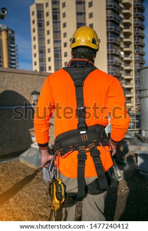 Picture showed the back side of male rope access worker dressing with industry fall protection yellow helmet abseiling safety body harness prior to work on construction site Sydney CBD, Australia  