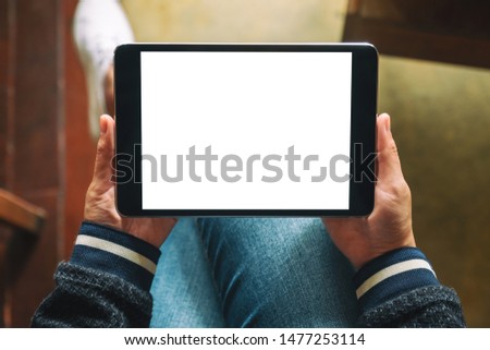 Top view mockup image of a woman holding black tablet pc with blank white screen while sitting in cafe