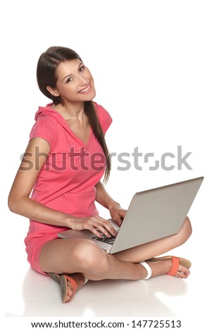 Smiling casual female sitting with laptop on the floor, isolated on white background