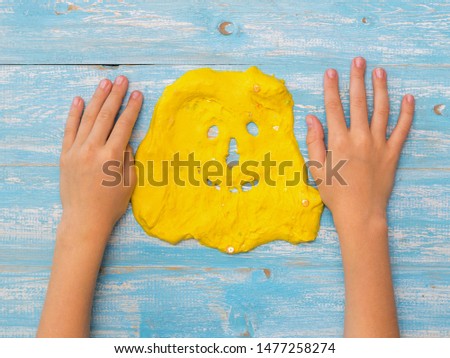 The child's hands on the table next to the face of a yellow slime. Toy antistress. Toy for the development of hand motor skills.