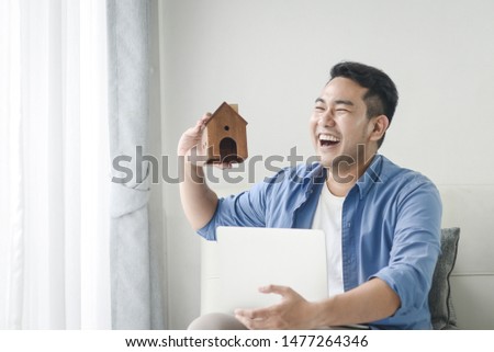 Asian man holding house in his hand and using laptop, real estate concept.