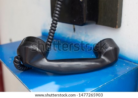 Vintage black telephone handset receiver hanging by the cord down