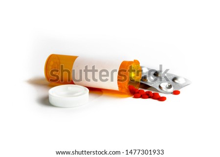A yellow plastic pill bottle with a blank label and a pill blister pack lying on the table with red pills spilled onto the table isolated on white