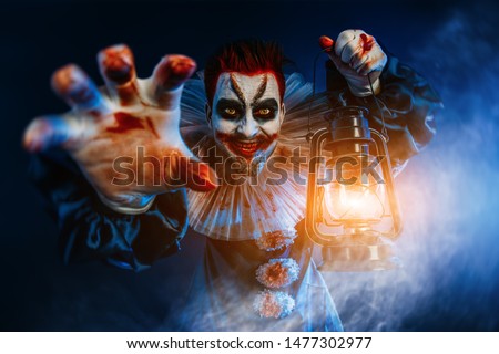 A portrait of an angry crazy clown from a horror film with a lantern. Halloween, carnival.