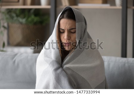 Unhealthy young woman feeling cold, covering in plaid, trying to get warm, sitting on couch in living room at home. Sick millennial girl suffering from high body temperature, caught cold or grippe. Royalty-Free Stock Photo #1477333994