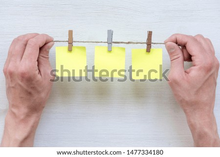 Blank stickers on a pins on rope in male hand on white wooden table background.