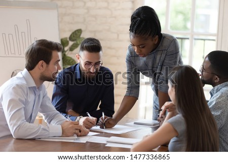 Serious african woman supervisor boss teach diverse staff workers explain project plan paperwork at group meeting, focused black female mentor training business team at corporate office briefing Royalty-Free Stock Photo #1477336865