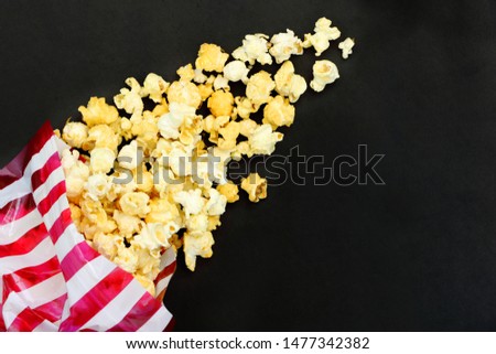 Top view isolated salted popcorn mix with cheese popcorn spilled from striped bag (red and white color) on black table background, movie cinema time concept, have copyspace
