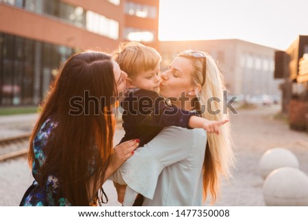 Portrait of the two cheerful young women who are kissing the little boy outdoors