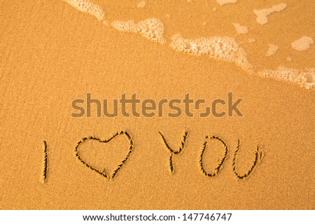I Love You text written by hand in sand on a beach.