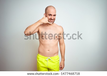 Young shirtless man on vacation wearing yellow swimwear over isolated background smiling doing phone gesture with hand and fingers like talking on the telephone. Communicating concepts.