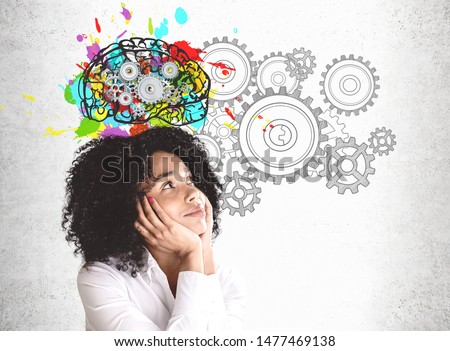 Smiling young African American woman in white shirt looking at colorful brain sketch with gears drawn on concrete wall. Concept of brainstorming Royalty-Free Stock Photo #1477469138