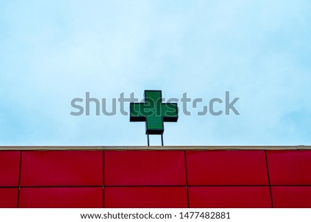 Green medical cross on the building against the blue sky. Neon green sign cross