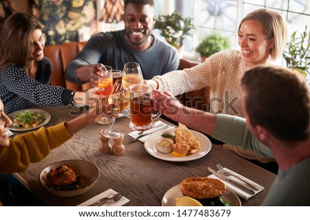 Friends Meeting For Meal In Traditional English Pub Making Toast Together Royalty-Free Stock Photo #1477483679