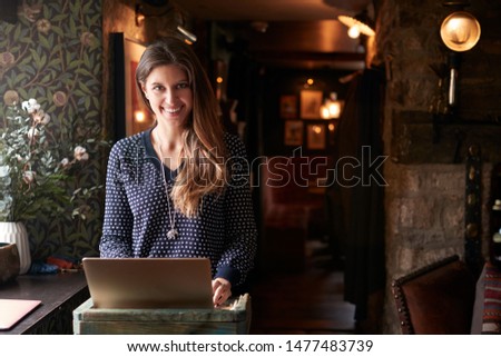 Portrait Of Female Receptionist Working On Laptop At Hotel Check In