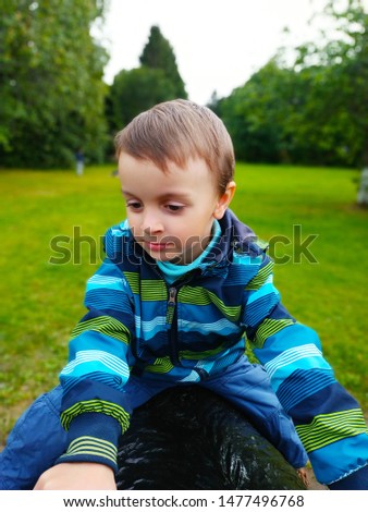 Little boy in a bright blue-green jacket on a background of green grass, foliage