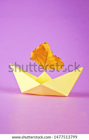 Yellow paper boat from origami with an autumn leaf on a purple background