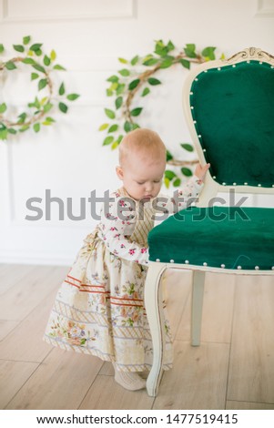 Cute little girl in a dress with a flower print  in the Easter decorations in the studio. Little girl with easter eggs and flowers in a spring studio
