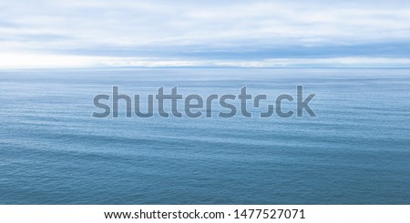 Aerial view over ocean horizon, ripples and waves in sea, wide scenic seascape, clouds in blue sky, top view high angle over water, simple subtle landscape background