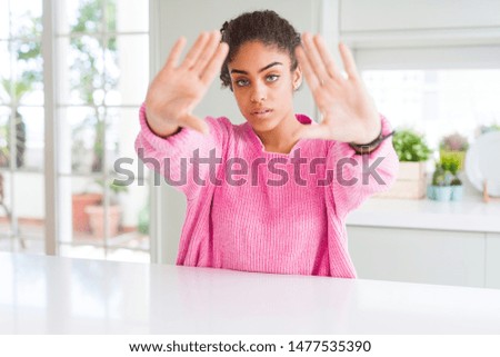 Beautiful african american woman with afro hair wearing casual pink sweater doing frame using hands palms and fingers, camera perspective