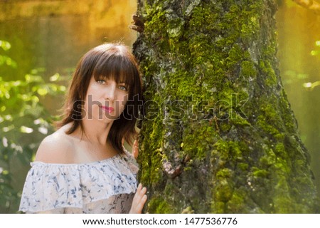 Portrait of a woman of thirty years at the trunk of a tree covered with moss, bright photo, portrait in the forest